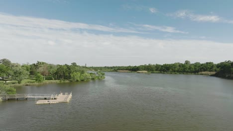 An-aerial-establishing-shot-of-Armand-Bayou-at-the-north-end-of-Bay-Area-Park-with-views-of-the-pier,-kayak-launch,-and-boat-ramp-under-blue-skies-with-thin-white-clouds-in-Pasadena,-Texas