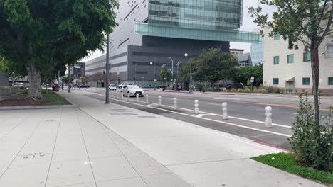 Pan-down-of-a-white-car-driving-down-the-street-with-a-skyscraper-in-the-back-drop-in-downtown-Los-Angeles