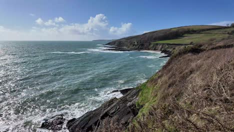Rugged-coast-of-Ireland-on-a-sunny-day-in-May-with-waves-and-green-fields,-wide-panorama