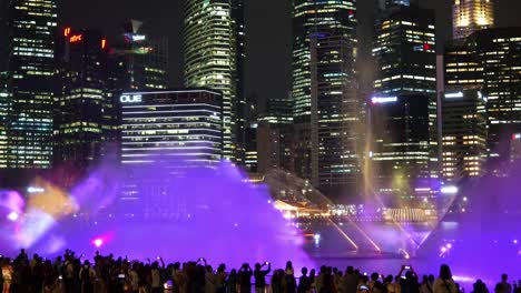 Magical-evening,-spectacular-visual-effect-SPECTRA-light-and-water-show-with-misty-spray-and-light-projects-against-downtown-cityscape,-time-lapse-shot-capturing-crowds-at-Marina-Bay-Sands-event-plaza