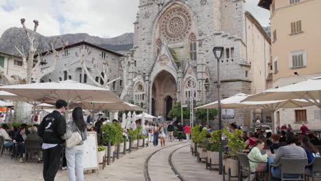 Bustling-cafe-terrace-in-Soller,-Mallorca-with-historic-church-backdrop