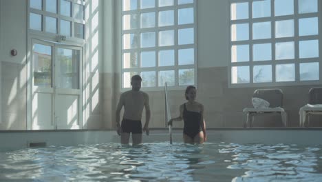 A-young-couple-in-black-swimsuits-go-down-the-steps-to-swim-in-the-spa's-heated-indoor-pool