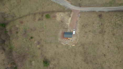 Aerial-perspective-of-a-small-house-under-construction-in-a-secluded-area,-with-a-white-van-parked-nearby