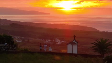 Tourists-at-Vigia-das-Baleias-viewpoint-enjoy-vibrant-sunset-over-ocean,-drone