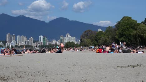 A-bikini-girl-shakes-a-blanket-at-a-beach-with-cityscape-of-Vancouver-and-mountains