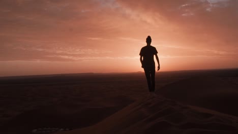Hombre-Marroquí-Caminando-En-La-Cima-De-Una-Duna-Disfrutando-Del-Amanecer-En-El-Desierto-Del-Sahara-Marroquí