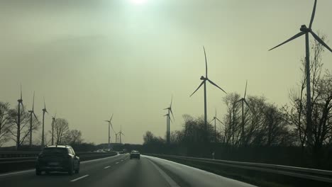 POV-Ansicht-Aus-Dem-Auto,-Die-Einen-Windpark-Mit-Modernen-Windmühlen-Zeigt,-Die-Sich-Bei-Sonnenlicht-Auf-Feldern-Drehen