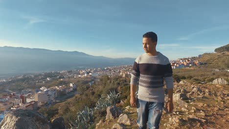 Die-Kamera-Folgt-Einem-Jungen-Marokkaner,-Der-An-Einem-Sonnigen-Tag-Auf-Den-Gipfel-Eines-Berges-In-Chefchaouen,-Marokko,-Geht