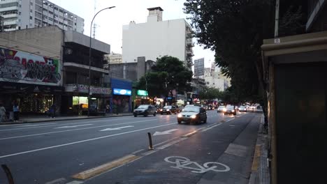 Lebhafter-Hyperlapse-Verkehr-Auf-Der-Corrientes-Avenue-In-Buenos-Aires,-Argentinien.-Autos-Fahren-Bei-Sonnenuntergang-Am-Nachmittag-Schnell,-Fahrradläden-Auf-Der-Straße-Und-Fußgänger,-Südamerika