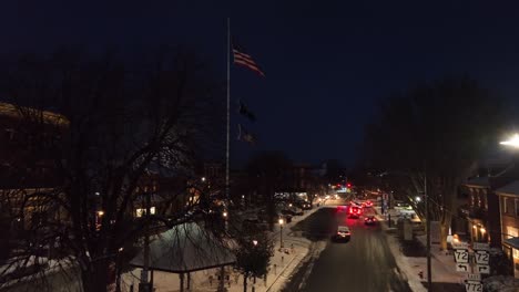 Town-square-with-American-flag-and-snow-covered-stores-at-night