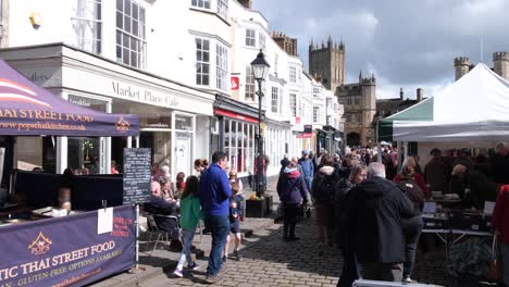 People-shopping-at-local-retail-shops-and-stalls-at-popular-Wells-Market-Place-on-a-busy-Easter-Weekend-in-Somerset,-Southwest-of-England-UK