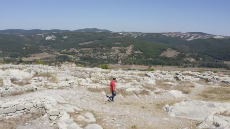 Orbiting-drone-shot-of-a-local-tourist-walking-around-the-ruins-of-the-ancient-city-of-Perperikon,-located-in-the-province-of-Kardzhali-in-Bulgaria