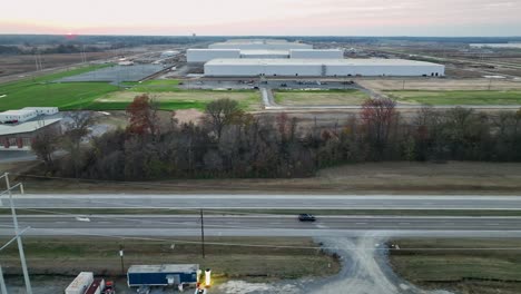 Aerial-following-vehicle-driving-in-front-of-Ford's-Megacampus,-BlueOval-City-at-Sunset-in-Stanton,-TN