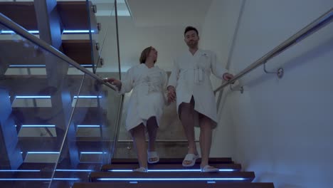 A-couple-holding-hands,-descends-the-illuminated-stairs-of-a-spa,-they-are-in-bathrobes