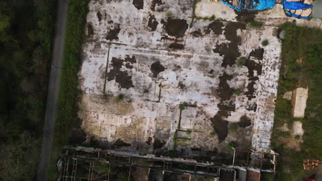 Derelict-concrete-foundation-near-abandoned-industrial-building,-aerial-top-down-view