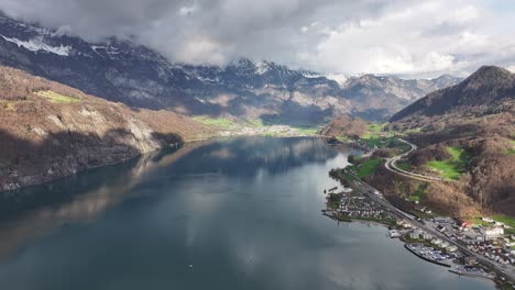 Luftaufnahme-Aus-Großer-Höhe-über-Den-Walensee-In-Der-Schweiz-Mit-Einer-Kulisse-Aus-Schneebedeckten-Bergen-Und-Einem-Malerischen-Wohngebiet-Entlang-Der-Uferbänke