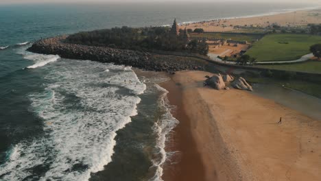 Luftaufnahme-Eines-Dolly-Rückflugs-über-Den-Wellen-Am-Strand-Mit-Enthüllung-Des-Küstentempels-In-Chennai