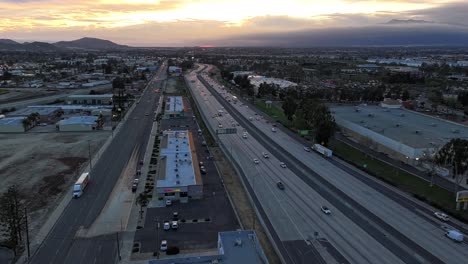 Unglaublich-Dynamischer-Sonnenuntergang-Mit-Wechselnden-Orange--Und-Rosafarbenen-Wolken-über-Dem-California-Highway-10-Mit-Geschäftigem-Verkehr,-Der-Bei-Sonnenuntergang-Immer-Dunkler-Wird.-Luftbild-Dolly-Push