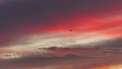 Großes-Frachtflugzeug-Fliegt-Durch-Leuchtend-Rosa-Flauschige-Wolken-Bei-Sonnenuntergang-Statisches-Teleobjektiv