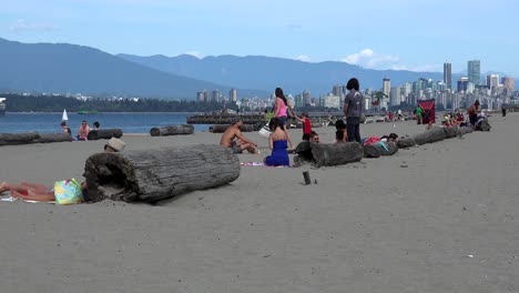 Una-Madre-Y-Su-Hijo-Caminando-Por-Una-Playa-De-Vancouver-Con-Un-Paisaje-Urbano-De-Vancouver-Y-Vistas-Al-Parque-Stanley-Al-Fondo