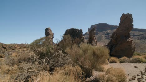 Eroded-volcanic-rocks-with-desert-shrubs-in-the-foreground,-Los-Roques-de-Garcia,-Teide-National-Park-in-Tenerife,-Canary-Islands-in-spring