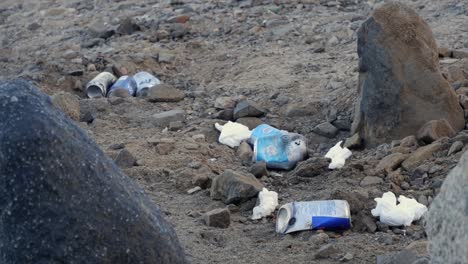 Pan-across-beer-cans-and-other-trash,-garbage-litter-on-beach-sand