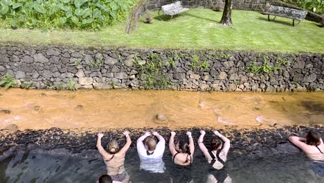 Some-people-enjoy-the-hot-thermal-waters-in-Dona-Beija,-Azores,-Portugal,-surrounded-by-lush-greenery-and-natural-beauty