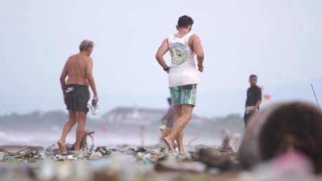 Tourists-run-in-the-morning-on-Kuta-Beach,-Bali,-which-is-very-dirty-with-rubbish
