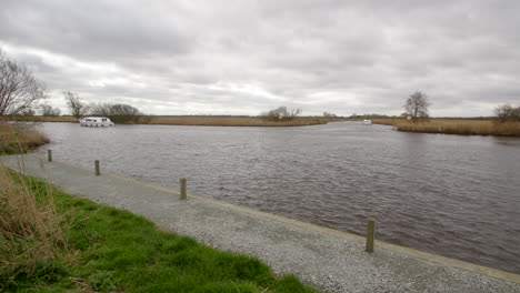 extra-wide-shot-of-the-river-Bure-with-a-white-Norfolk-Broads-cruisers-boat-passing-the-entry-to-South-Walsham-Broad