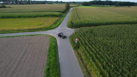 Ein-Schwarzer-Oldtimer-Wendet-An-Einer-Kreuzung-Neben-Vielen-Feldern