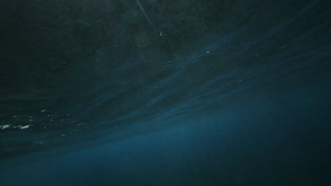 Moody-grey-rubble-coral-reef-with-ocean-water-glistening-and-shining-as-wave-creates-barrel,-view-from-behind