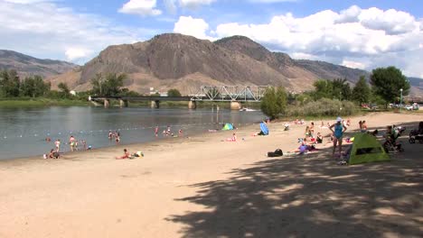 Kamloops-river-beach-with-speedboat-and-tent,-people-looking-at-tend