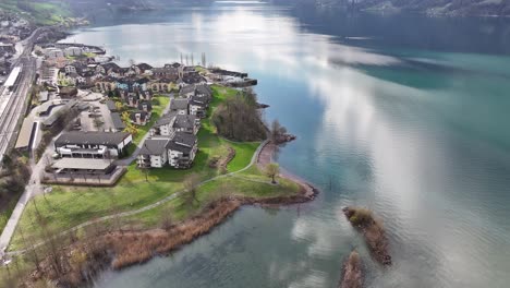 Nestled-by-Lake-Walenssee-in-Switzerland,-a-residential-district-lines-the-shoreline,-with-railway-tracks-meandering-through-the-quaint-village-settlement-of-Murg