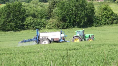 A-green-tractor-pulls-a-blue-tank-behind-it-and-fertilizes-the-field-in-Sauerland