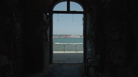 View-of-a-speedboat-passing-by-from-inside-an-abandoned-alley-in-Lisbon,-Portugal