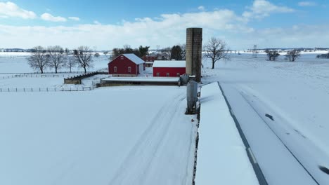 Luftaufnahme-Einer-Ländlichen-Schneebedeckten-Landschaft-Mit-Einer-Roten-Scheune,-Einem-Silo-Und-Zaunlinien