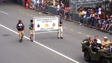 Veteranos-Y-Familias-Viajan-En-Un-Vehículo-Militar-Antiguo-Con-Remolque,-Conduciendo-Por-La-Calle,-Participando-En-El-Desfile-Del-Día-De-Anzac