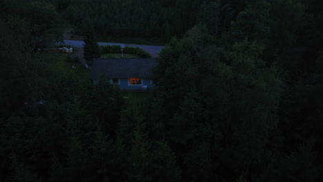 Aerial-view-toward-a-house-with-a-light-inside,-gloomy-evening-in-middle-of-forest