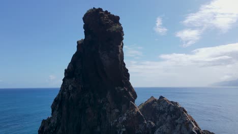 Luftaufnahmen-Einer-Drohne-Fangen-Einen-Atemberaubenden-Berggipfel-Mit-Blick-Auf-Den-Ozean-Ein,-Während-Vögel-Anmutig-Durch-Den-Weiten-Blauen-Himmel-Schweben