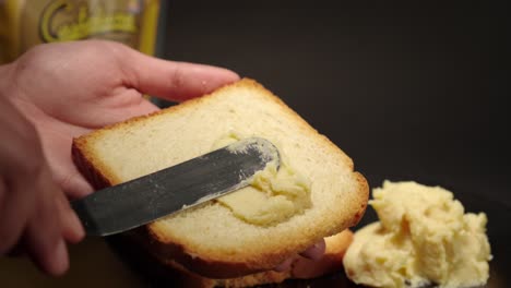 Butter-cheese-smooth-soft-creme-peanut-jelly-putting-on-top-of-a-toast-of-bread-slice-slow-motion-with-black-background-female-hands