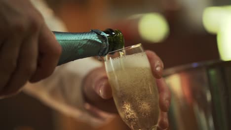 Die-Hände-Des-Mannes-Halten-Eine-Grüne-Flasche-Und-Gießen-Champagner-In-Ein-Glas-Zum-Feiern