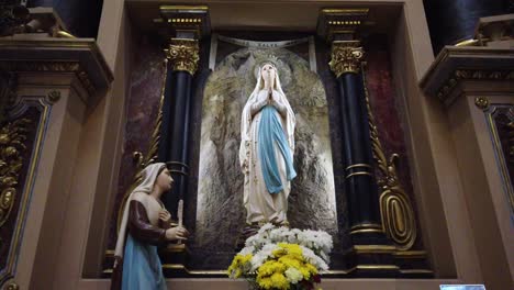 Virgin-Mary-of-the-saint-conception-basilica-at-latin-american-church-sculpture-of-classic-virginal-statue-white-and-light-blue-with-sisters-praying-on-her-knees