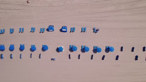 Luftaufnahme-Des-Strandes-Mit-Blauen-Stühlen-Und-Sonnenschirmen,-Blauem-Wasser,-Blauem-Himmel,-Palmen,-Ft