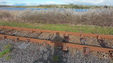 Sombra-De-Ciclista-Y-Bicicleta-Sobre-Vías-De-Ferrocarril-Con-Río-Y-Flor-En-Waterford-Greenway-Irlanda