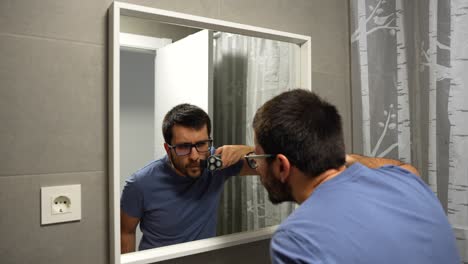 Man-shaving-off-moustache-with-electric-shaver,-mirror-reflection