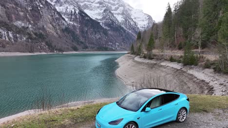 Electric-blue-Tesla-Model-3-on-Alpine-lakeside-road,-Klöntalersee-Switzerland