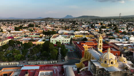Aerial-view-backwards-over-the-Parque-Juárez-and-the-San-Luis-Obispo-Baroque,-sunset-in-Huamantla,-Mexico