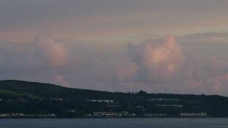 Timelapse-pink-clouds-passing-over-water-and-land-and-distant-town-in-summer