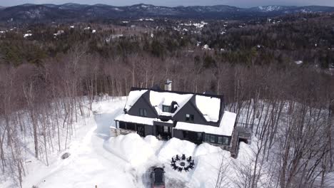 Aerial-shot-panning-down-to-a-snow-covered-Luxury-Chalet-in-winter-with-black-SUV-parked-in-front