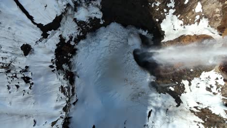 Top-down-shot-of-waterfall-from-melting-snow,-drone-ascending-revealing-size-of-waterfall